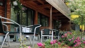 Una baita di legno con veranda, posti a sedere all'aperto e un giardino con fiori rosa.