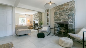 A living room with a stone wall, a fireplace, a sofa, a chair, and a coffee table. - Hendre - sleeps 8 guests  in 4 bedrooms (Menai Bridge)