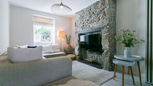 A living room with a stone fireplace, a sofa, a television, and a small table with a plant. - Hendre - sleeps 8 guests  in 4 bedrooms (Menai Bridge)