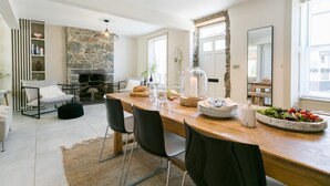 A dining area with a stone fireplace, a wooden table set for a meal, and a cozy seating arrangement. - Hendre - sleeps 8 guests  in 4 bedrooms (Menai Bridge)