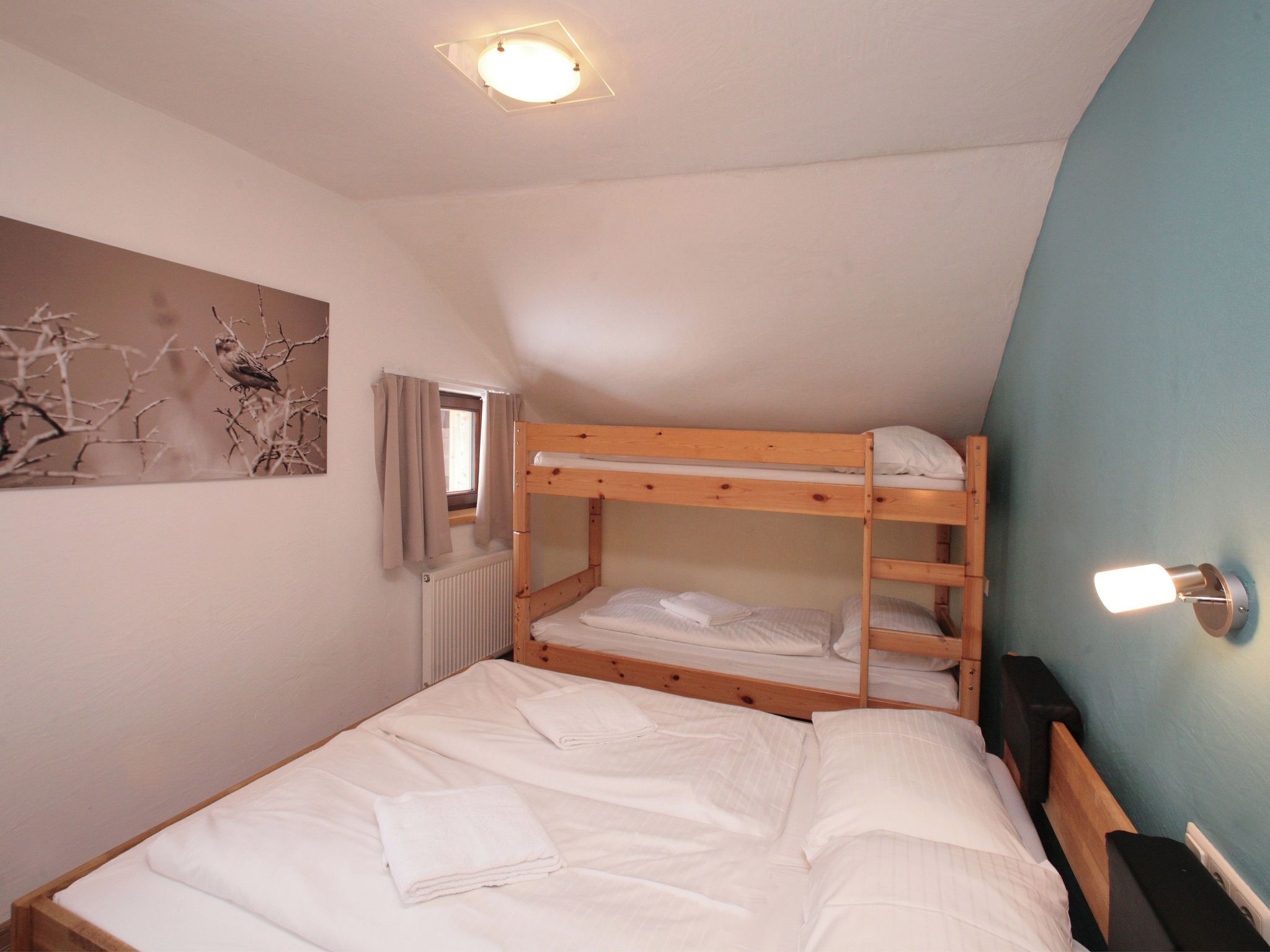 Een slaapkamer met stapelbed, een radiator, een raam met gordijnen en een wandlamp.