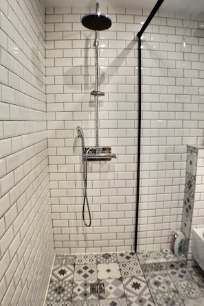 A shower with a handheld showerhead and a wall-mounted faucet, tiled with white and patterned tiles.