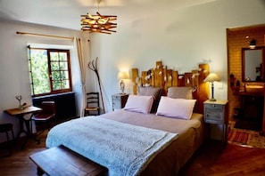 A bedroom with a bed, bedside lamps, a window with curtains, a desk with a chair, and a mirror.