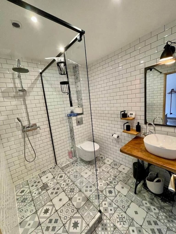 A modern bathroom with a glass shower enclosure, a white toilet, and a wooden vanity with a large sink.