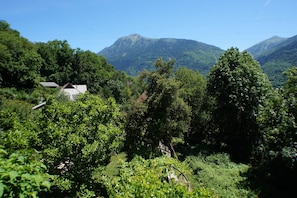 A mountainous landscape with dense greenery and a small building with a sloped roof.
