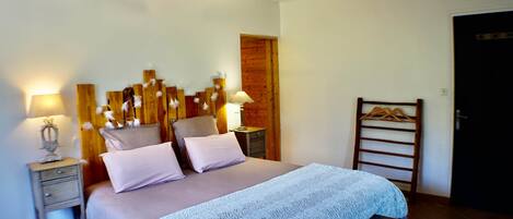 A bedroom with a bed, bedside tables, a hanging light fixture, a wooden headboard, a wooden door, and a wooden bench.