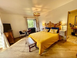 A bedroom with a large bed, a desk, a chair, and a window.