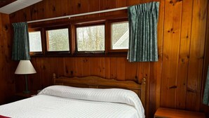 A wooden-paneled room with a bed, a nightstand, and a dresser.