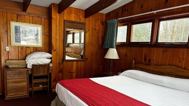 A wooden room with a bed, a desk, a chair, a lamp, and a mirror.