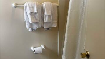 A bathroom with a toilet, a small trash bin, a towel rack with folded towels, and a shower curtain.