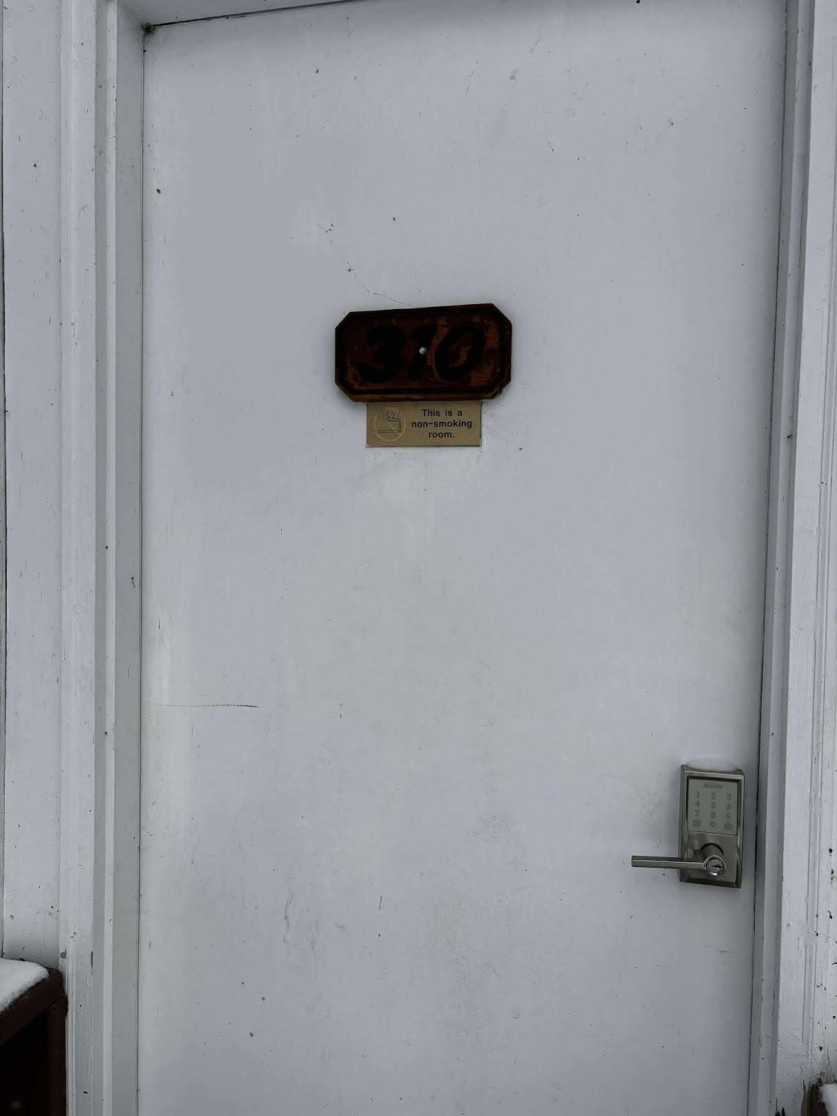 A white door with a non-smoking sign and a metal plate with numbers.