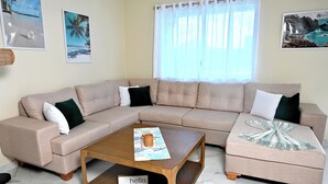 Una sala de estar con un sofá seccional color beige, una mesa de centro de madera con un posavasos, y un letrero que dice 'hello'.