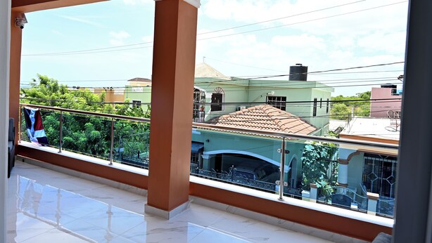 Un balcón con vista a casas vecinas y suelo de baldosas.