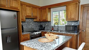 Una cocina con gabinetes de madera, encimeras de granito, refrigerador, estufa, microondas y una ventana con vista a zonas verdes.