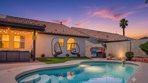 Une maison avec une piscine, un espace salon extérieur et un ciel au coucher du soleil.