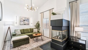 Un salon moderne avec un canapé vert, une table basse ronde, une cheminée et une grande fenêtre avec des rideaux.