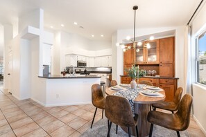 A modern kitchen with white cabinets, a central island, and a dining area with a round table and chairs. - Family Resort Home: Pool, Game Room & Mountain Views — Sleeps 12, EV Charging (Las Vegas)
