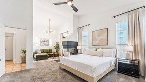 Une chambre spacieuse avec un grand lit, un ventilateur de plafond, une télévision et une vue sur l’extérieur.