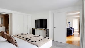 A bedroom with a bed, a TV on a stand, a wardrobe, and an open door leading to another room. - Champs-elysees Apartment for 6 Guests (Paris)