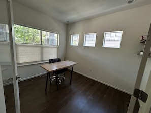 Um quarto com uma mesa, cadeiras, três janelas e uma porta.