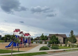 Ein Spielplatz mit Klettergerüsten und einer Rutsche, umgeben von einer Wohngegend mit Häusern und Grünflächen.