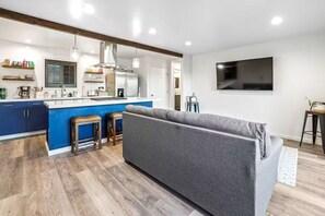 A modern kitchen with a blue island, a grey sofa, and a TV mounted on the wall. - Uncork & Unwind in Paso Robles Wine Country (Paso Robles)
