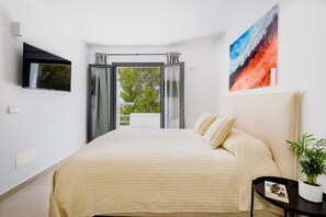 A bedroom with a bed, a TV, a painting, and a view of greenery outside. - OFFER Villa Romero Luxury | Ibiza Art House (Sant Rafel De Sa Creu/Sant Rafel De La Creu)