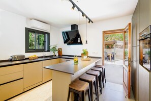 A modern kitchen with a central island, bar stools, a built-in oven, and a large window. - OFFER Villa Romero Luxury | Ibiza Art House (Sant Rafel De Sa Creu/Sant Rafel De La Creu)