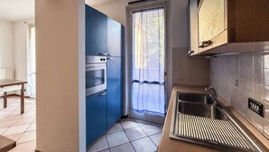 A kitchen with blue cabinets, a stainless steel oven, a sink, and a window with a curtain. - MeLaChillo (Azzate)