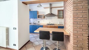 A modern kitchen with a wooden table and two bar stools, blue cabinets, and a brick wall. - MeLaChillo (Azzate)