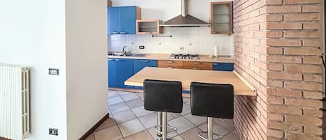 A modern kitchen with a wooden table and two bar stools, blue cabinets, and a brick wall.