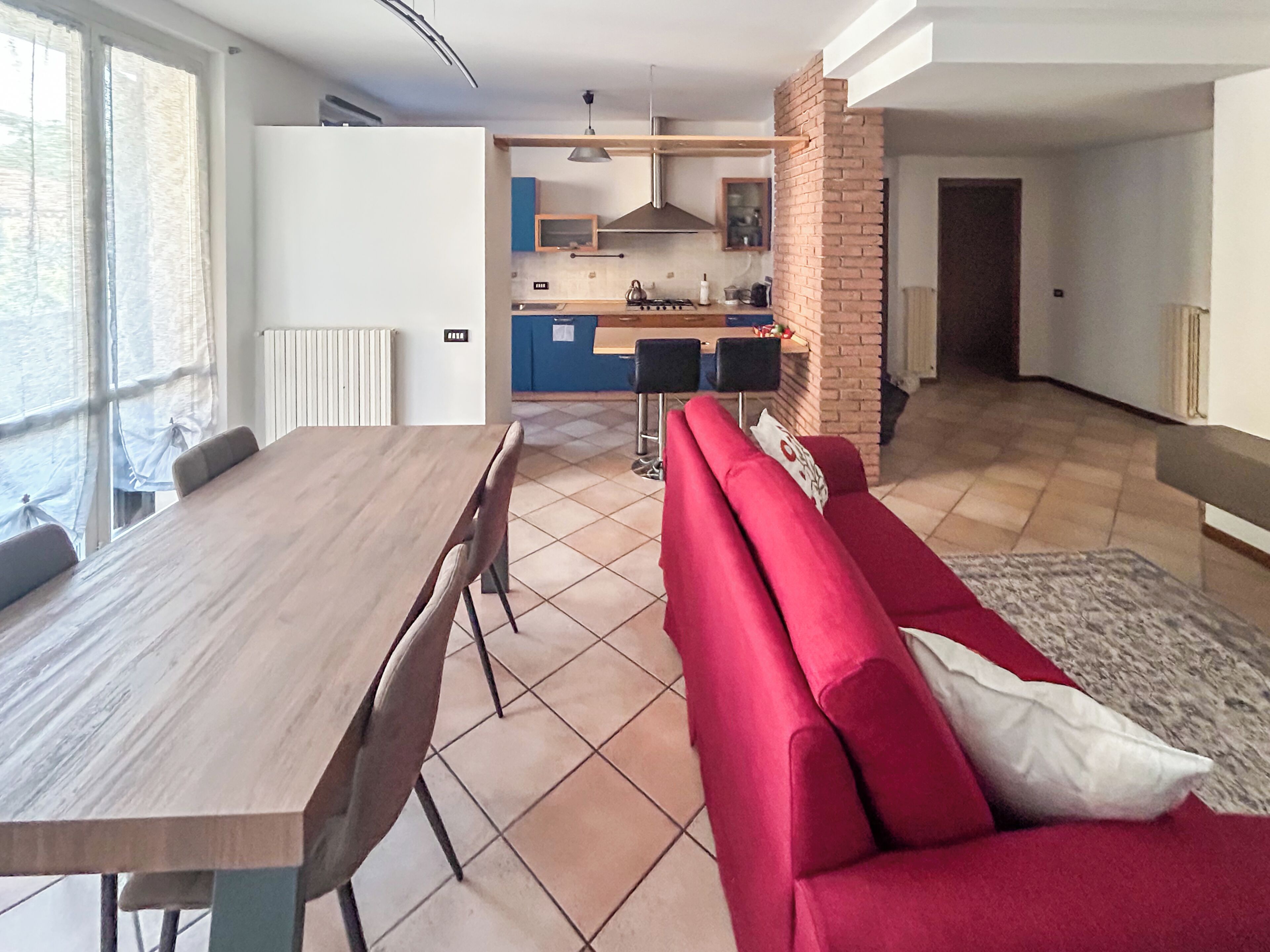 A modern kitchen with a central island, a dining area with a wooden table and chairs, and a red sofa with a patterned rug.