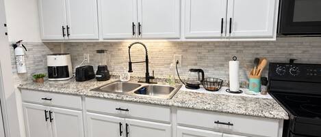 Una cocina moderna con armarios blancos, encimeras de granito, una estufa negra y un lavamanos de acero inoxidable.