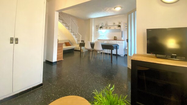 A modern living room with a TV, a staircase leading to a kitchen, and a dining area. - CASA MARGARIDA - LÈSCALA - 20 meters from Riells Beach, with parking and a barbecue (L'Escala)