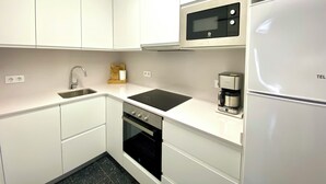 A compact kitchen with white cabinetry, a built-in microwave, a coffee maker, and a refrigerator. - CASA MARGARIDA - LÈSCALA - 20 meters from Riells Beach, with parking and a barbecue (L'Escala)
