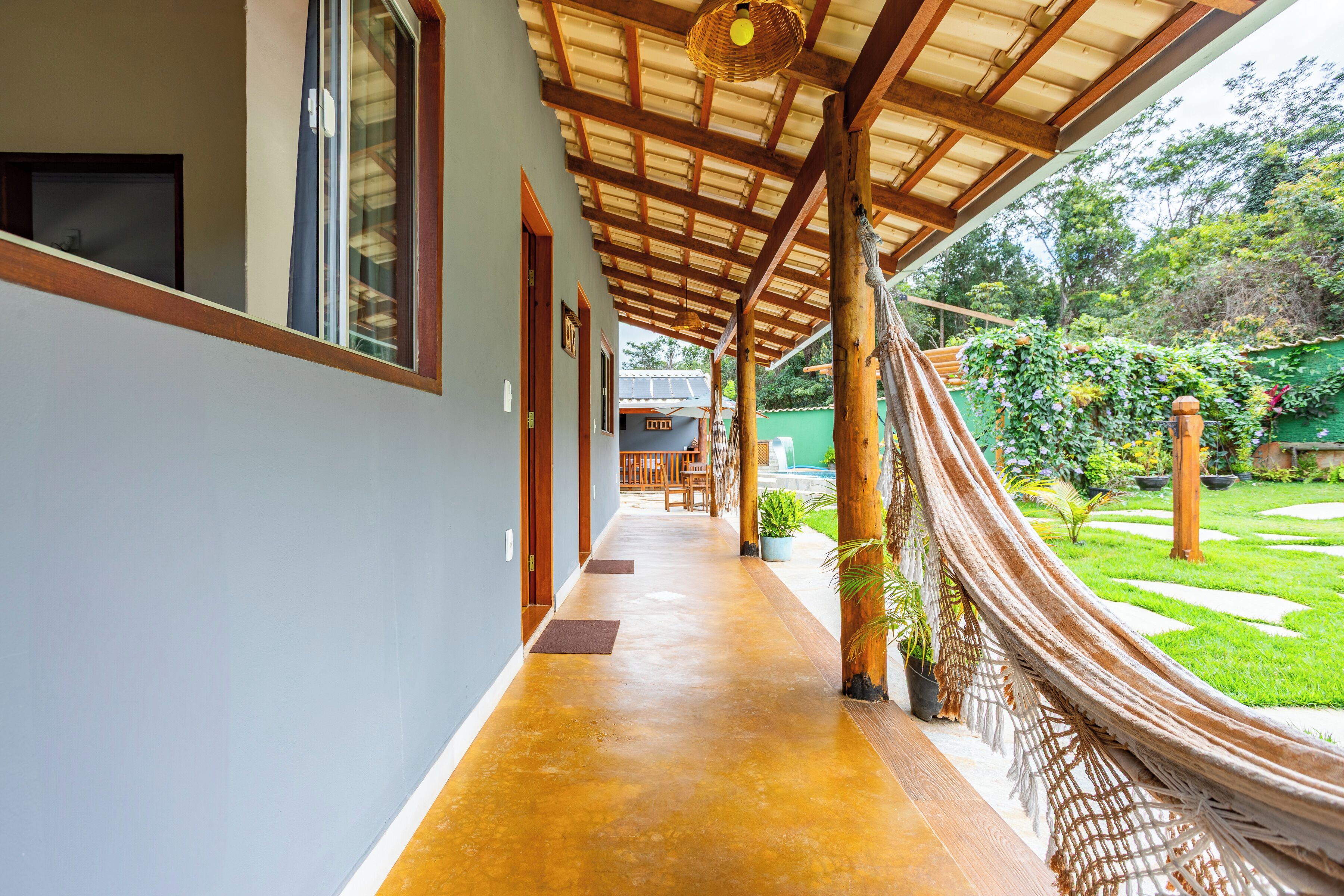 A covered corridor with a concrete floor, wooden beams, and a view of a garden.