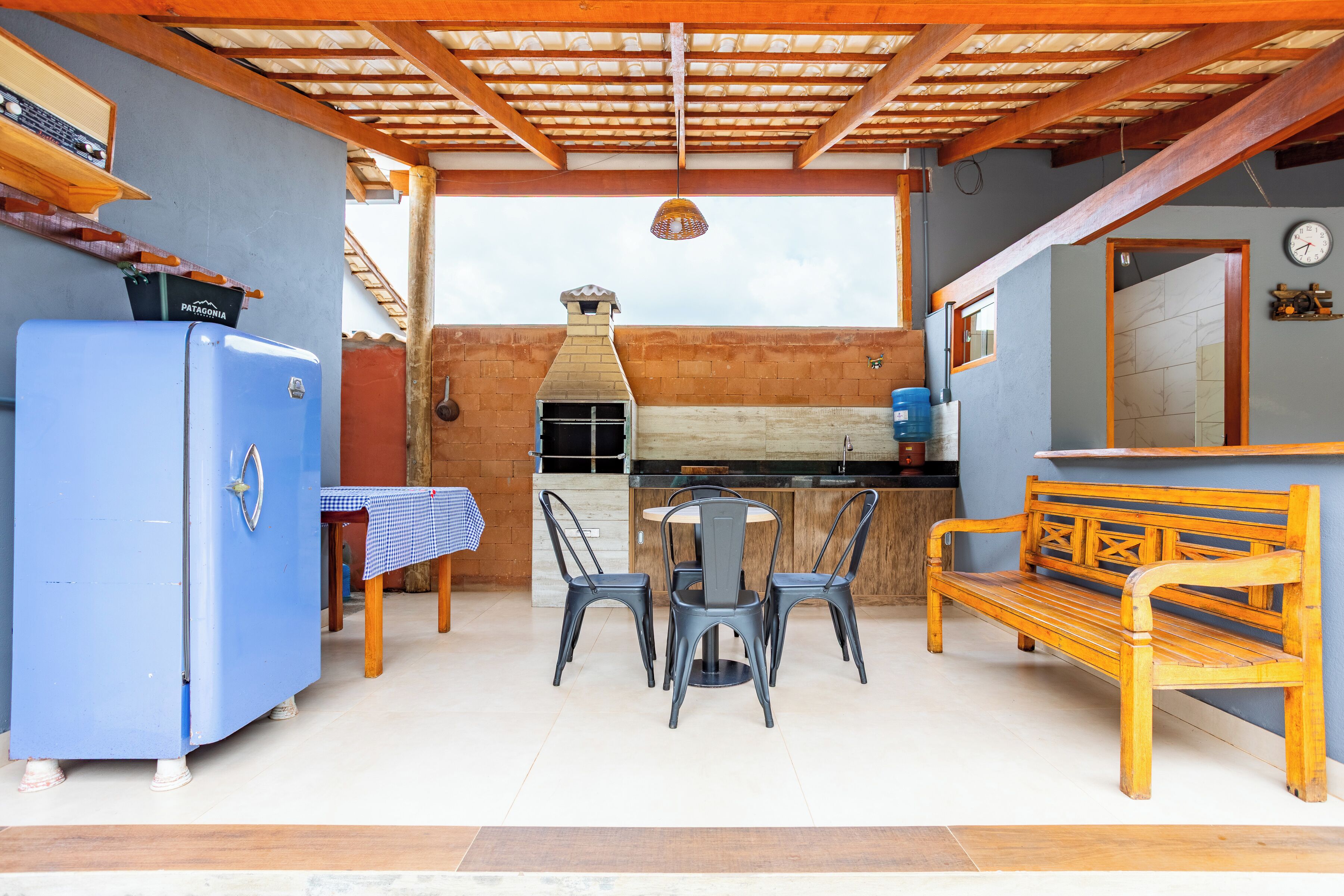 A patio area with a blue refrigerator, a wooden bench, and a table with chairs.
