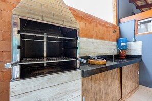 A brick oven grill with a metal rack, a water dispenser, and a cutting board on a black countertop. - Recanto Oliveira (Pirenópolis)