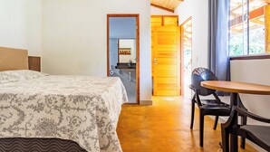 Ein Schlafzimmer mit Bett, Holzboden, einem durchgehenden Türspalt sichtbaren Badezimmer und einem Essbereich mit Tisch und Stühlen.