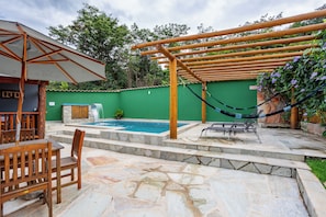 Un área de piscina con una pérgola de madera, una hamaca y un espacio de descanso con mesa y sillas.