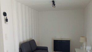 Ett modernt vardagsrum med en grå soffa, ett litet sidobord, ett vitt skrivbord och ett mörkblått skåp.