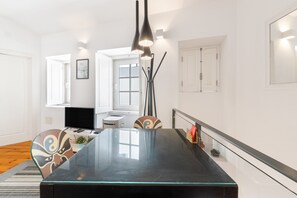 Uma sala de jantar moderna com mesa de vidro, cadeiras e luminária pendente preta.