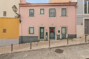 A pink building with multiple windows and a green door, situated on a cobblestone street. - Madragoa Boutique Studio (Lisbon)