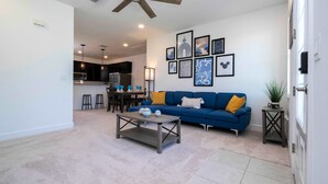 A living room with a blue sofa, a coffee table, and artwork on the wall. - Bright 4BR w PS4   Mickey Rooms at Holly Village  132 (Davenport)