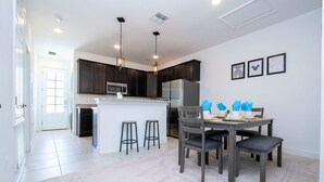 A modern kitchen with dark cabinets, a central island, bar stools, and a dining table set for four. - Bright 4BR w PS4   Mickey Rooms at Holly Village  132 (Davenport)