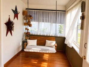 Una habitación con un banco de madera, cojines blancos, una cesta colgante y un adorno con forma de estrella en la pared.