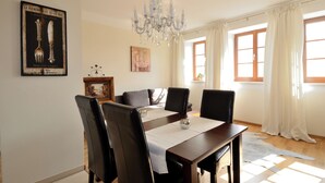 Une salle à manger avec un lustre, une table entourée de chaises et un tableau accroché au mur.