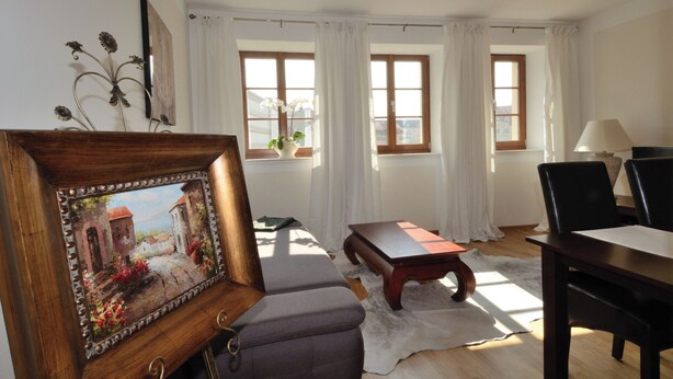 Une pièce comprenant un canapé, une table, une chaise, un tableau et une fenêtre avec des rideaux.
