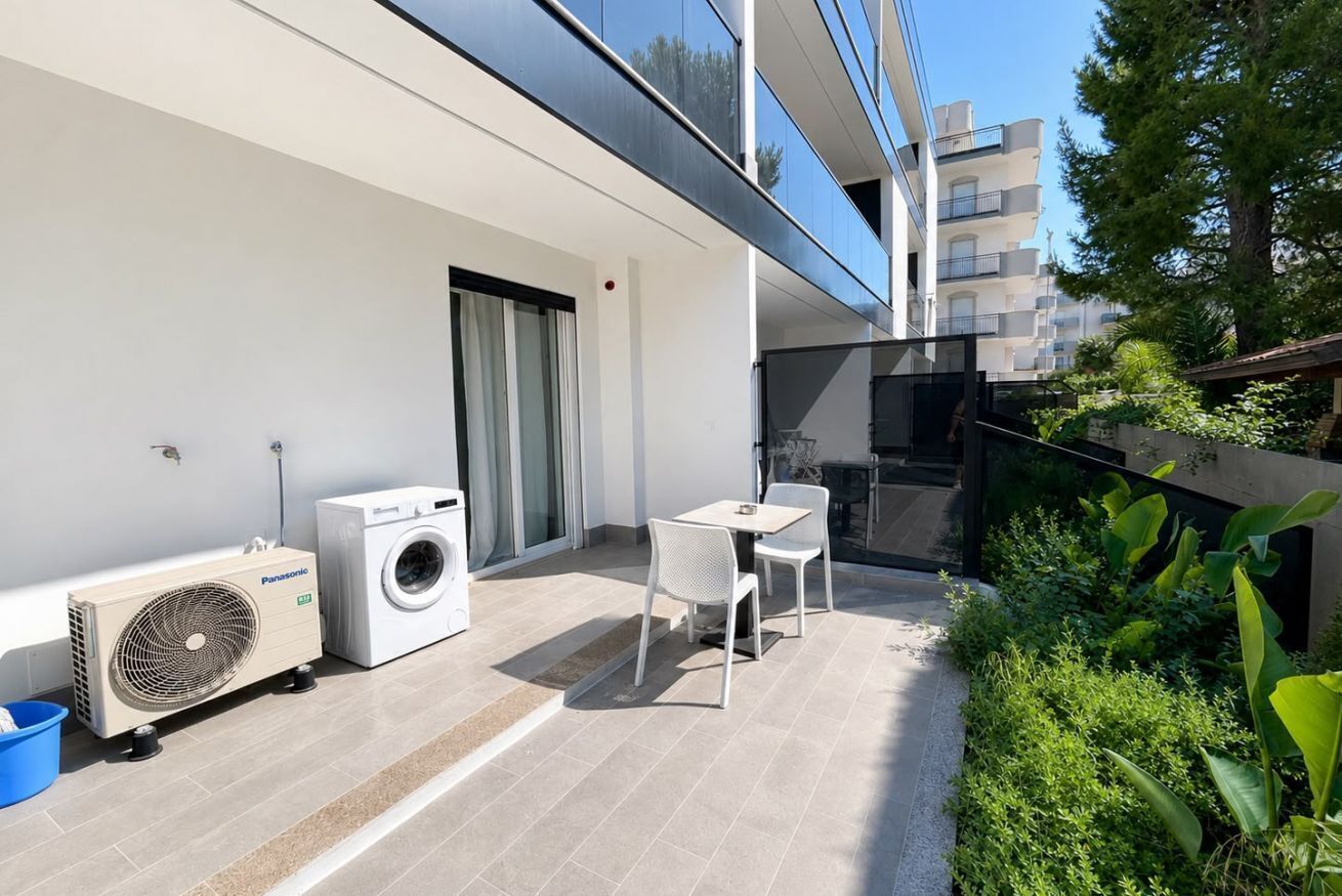 A balcony with a washing machine, a fan, and a table with chairs.