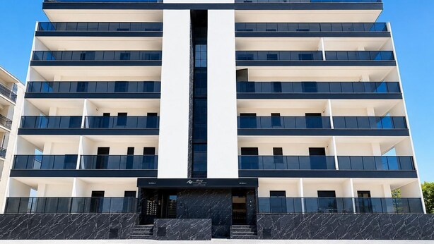 Un immeuble à plusieurs étages doté d’une entrée centrale, de balcons à chaque étage et surplombant un ciel dégagé.